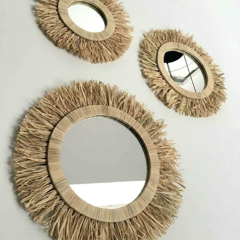 May include: Three round mirrors with natural woven straw frames. The mirrors are different sizes and are arranged in a staggered pattern on a white wall.