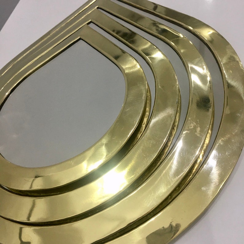 May include: A gold-toned, layered, decorative mirror with a teardrop shape. The mirror has a polished, reflective surface.