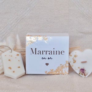 Op de afbeelding: Een verzameling witte kaarsen met goudblad accenten. Bevat een tag-vormige kaars, een doos met de tekst "Marraine en or", en een hartvormige kaars met een houten lont en gedroogde bloemen.