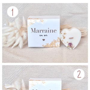Op de afbeelding: De afbeelding toont twee cadeau-opties. Elke optie bevat een witte doos met gouden accenten en de tekst "Marrine en or", en een hartvormige kaars. E&eacute;n optie heeft een rechthoekige kaars.