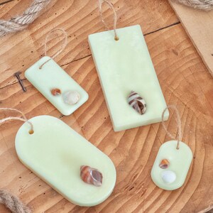 Op de afbeelding: Vier lichtgroene rechthoekige en ovale wasmelts met ingebedde schelpen. De wasmelts hangen aan een touwtje.
