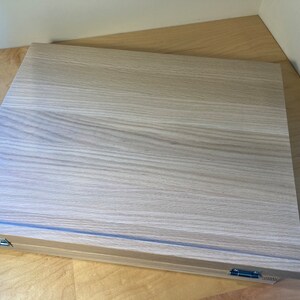 K&ouml;nnte beinhalten: Eine Aufbewahrungsbox aus hellem Holz mit einem Scharnierdeckel. Die Box hat eine helle Holzmaserung und einen dezenten Glanz.
