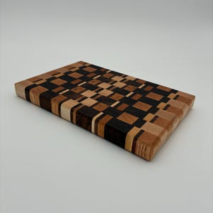 Op de afbeelding: Een rechthoekige snijplank opgebouwd uit een moza&iuml;ek van kleine, meerkleurige houten blokjes. Het oppervlak heeft een geometrisch patroon van lichtbruine, middenbruine en donker espresso-kleurige houten stukjes in een raster.