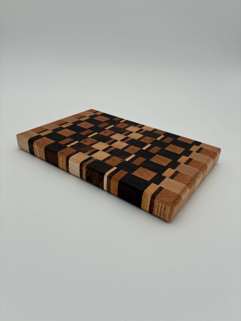 Op de afbeelding: Een rechthoekige snijplank opgebouwd uit een moza&iuml;ek van kleine, meerkleurige houten blokjes. Het oppervlak heeft een geometrisch patroon van lichtbruine, middenbruine en donker espresso-kleurige houten stukjes in een raster.