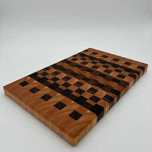 Op de afbeelding: Een rechthoekige houten snijplank met een kops houten constructie, voorzien van een moza&iuml;ekpatroon van kleine, afwisselende vierkantjes in tinten lichtbruin, middenbruin en donker espressohout, wat een complex rasterontwerp vormt.