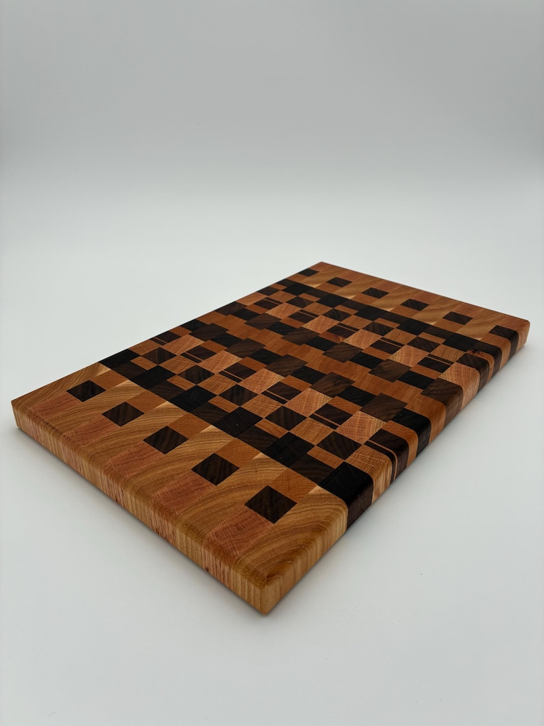 Op de afbeelding: Een rechthoekige houten snijplank met een kops houten constructie, voorzien van een moza&iuml;ekpatroon van kleine, afwisselende vierkantjes in tinten lichtbruin, middenbruin en donker espressohout, wat een complex rasterontwerp vormt.