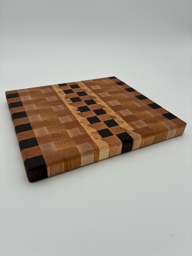 Op de afbeelding: Een vierkante houten snijplank met een kops houten constructie en een veelkleurig dambordpatroon. Het ontwerp bevat afwisselende blokken van lichtbruin, medium bruin en donker espressokleurig hout in een rasterpatroon.