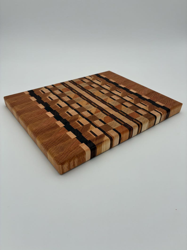 Op de afbeelding: Een rechthoekige houten snijplank met een kops houten constructie en een complex geometrisch patroon. Het oppervlak toont een moza&iuml;ek van lichte, middelbruine en donkerbruine houttinten die in afwisselende blokken zijn gerangschikt.