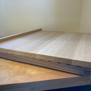 K&ouml;nnte beinhalten: Ein helles Holz-Schneidebrett mit erh&ouml;htem Rand und einer Reihe von Rillen entlang der Unterkante.