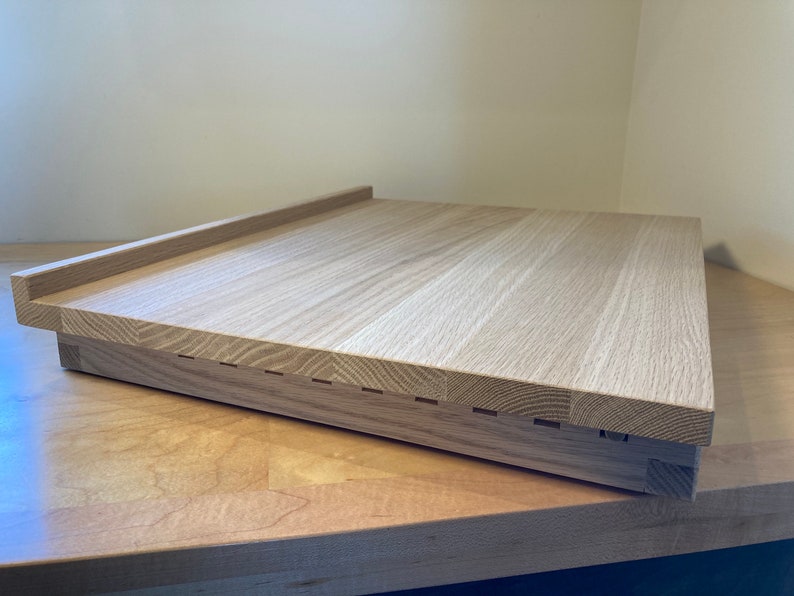 K&ouml;nnte beinhalten: Ein helles Holz-Schneidebrett mit erh&ouml;htem Rand und einer Reihe von Rillen entlang der Unterkante.