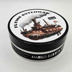 May include: A round black and white tin container labeled Mango Butter Shaving Soap. The lid features a detailed illustration of a steamship with smoke, the text Flying Dutchman, and a small logo for Talent Soap Factory on a white background.