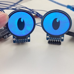 Può includere: Due display LED rotondi blu con una forma di occhio nera al centro. I display sono montati su schede a circuito con pin sul fondo.