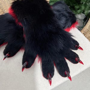 May include: A pair of black faux fur gloves with red accents and long, pointed, red-tipped claws. The gloves are designed to resemble animal paws, with a furry texture and a detailed claw design.