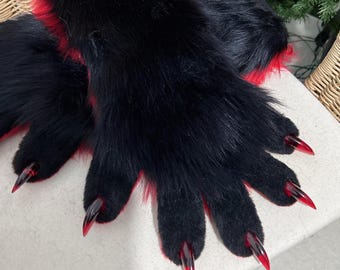 May include: A pair of black faux fur gloves with red accents and long, pointed, red-tipped claws. The gloves are designed to resemble animal paws, with a furry texture and a detailed claw design.