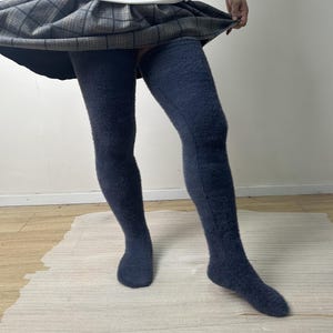 May include: A pair of dark charcoal grey thigh-high socks with a fuzzy, textured knit finish. The socks extend above the knee and are paired with a grey and black plaid pleated skirt that sits at the upper thigh, showing the full length of the socks.