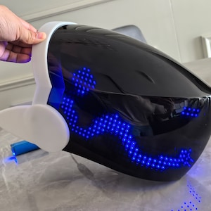 May include: A black helmet with a white visor and blue LED lights. The lights are arranged in a pattern that resembles a wave.