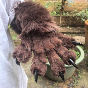 May include: Brown furry monster paw gloves with long black claws. The gloves have a realistic design with detailed fur texture. The claws are sharp and pointed, adding to the overall monster aesthetic. Perfect for cosplay or costume parties.