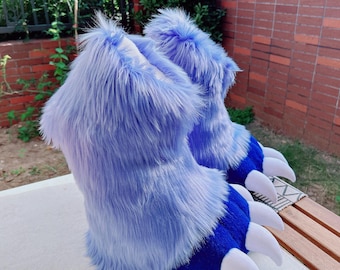 May include: A pair of furry, blue monster feet. The boots are a light blue with darker blue accents on the toes and white claws. The boots are made of a soft, plush material.