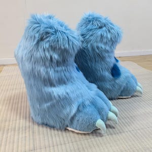 May include: A pair of light blue monster feet, with long, shaggy fur and large claws. The boots are designed to look like monster feet, with a round, padded shape and a white sole.