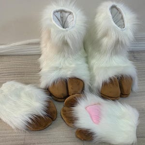 May include: A set of white furry costume feet and hand covers. The feet are boots with brown hooves. The hand covers are white with brown hooves and a pink accent. The costume pieces are designed to resemble an animal.