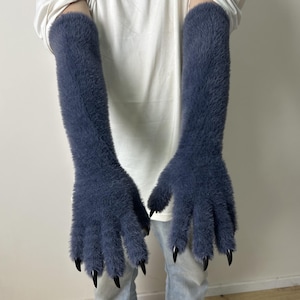 May include: A pair of long, dark blue fuzzy gloves reaching past the elbows. The gloves feature a thick, soft, faux-fur texture and are finished with sharp, pointed black claw-like tips on each of the five fingers, creating a distinct look.