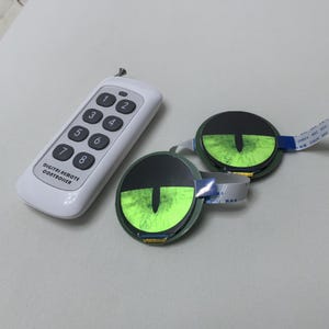 May include: A white digital remote controller with numbered buttons and the text "DIGITAL REMOTE CONTROLLER." Two circular devices with green eye-like displays and attached cables are also present.