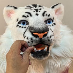 May include: White plush tiger head with blue eyes and a black nose. The mouth is open and shows white teeth. The fur is soft and fluffy.