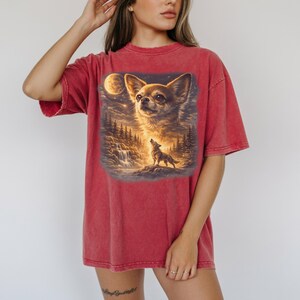 May include: Red t-shirt featuring a detailed graphic of a Chihuahua with a full moon and a howling wolf in a forest setting. The shirt has short sleeves and a relaxed fit.