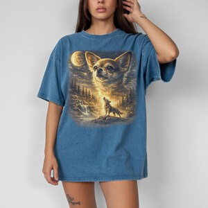 May include: Blue t-shirt featuring a detailed graphic of a Chihuahua dog with a full moon and a howling wolf in a forest scene. The artwork has a painterly style with warm, golden tones and a touch of fantasy.