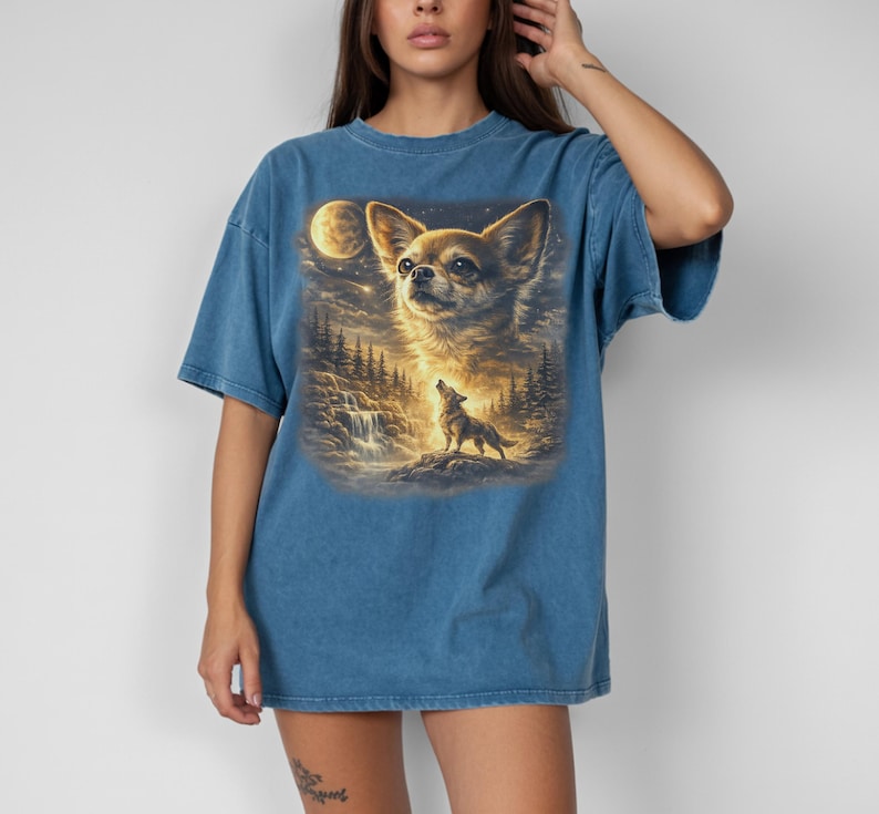 May include: Blue t-shirt featuring a detailed graphic of a Chihuahua dog with a full moon and a howling wolf in a forest scene. The artwork has a painterly style with warm, golden tones and a touch of fantasy.