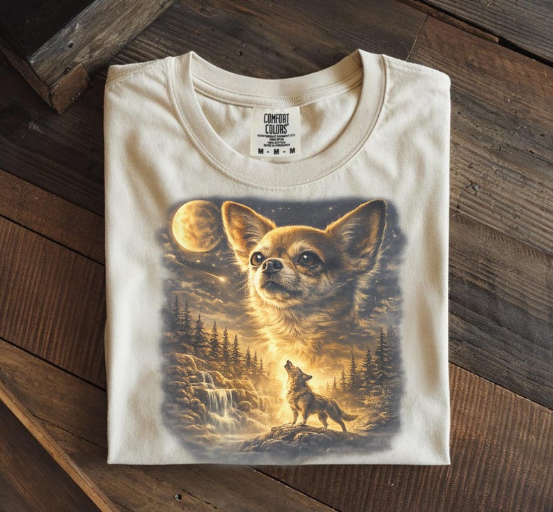 May include: Cream-colored t-shirt featuring a detailed illustration of a Chihuahua dog with a full moon and a howling wolf in a forest scene. The shirt is made of a soft material and has a Comfort Colors tag.