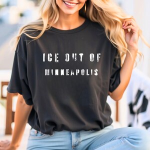 Puede incluir: Camiseta negra con el texto blanco "ICE OUT OF MINNEAPOLIS" en letras desgastadas. La camiseta es de color oscuro y parece estar hecha de un material suave. La camiseta es de estilo casual.