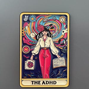 May include: A vibrant magnet with an illustration of a person in a white blouse and red trousers. The design includes swirling colours, flowers, books, and the text "THE ADHD". The magnet has a yellow border.