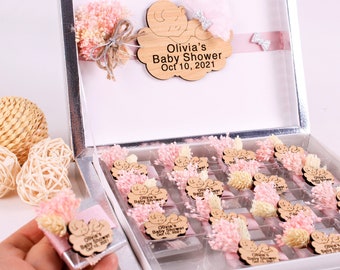 May include: A silver box filled with small gift boxes decorated with pink and white dried flowers and a wooden cloud with the text "Olivia's Baby Shower Oct 10, 2021".