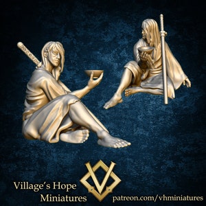 May include: Two golden figurines of people sitting with bowls in their hands. One figure is holding a sword. The figures are painted in a gold color.