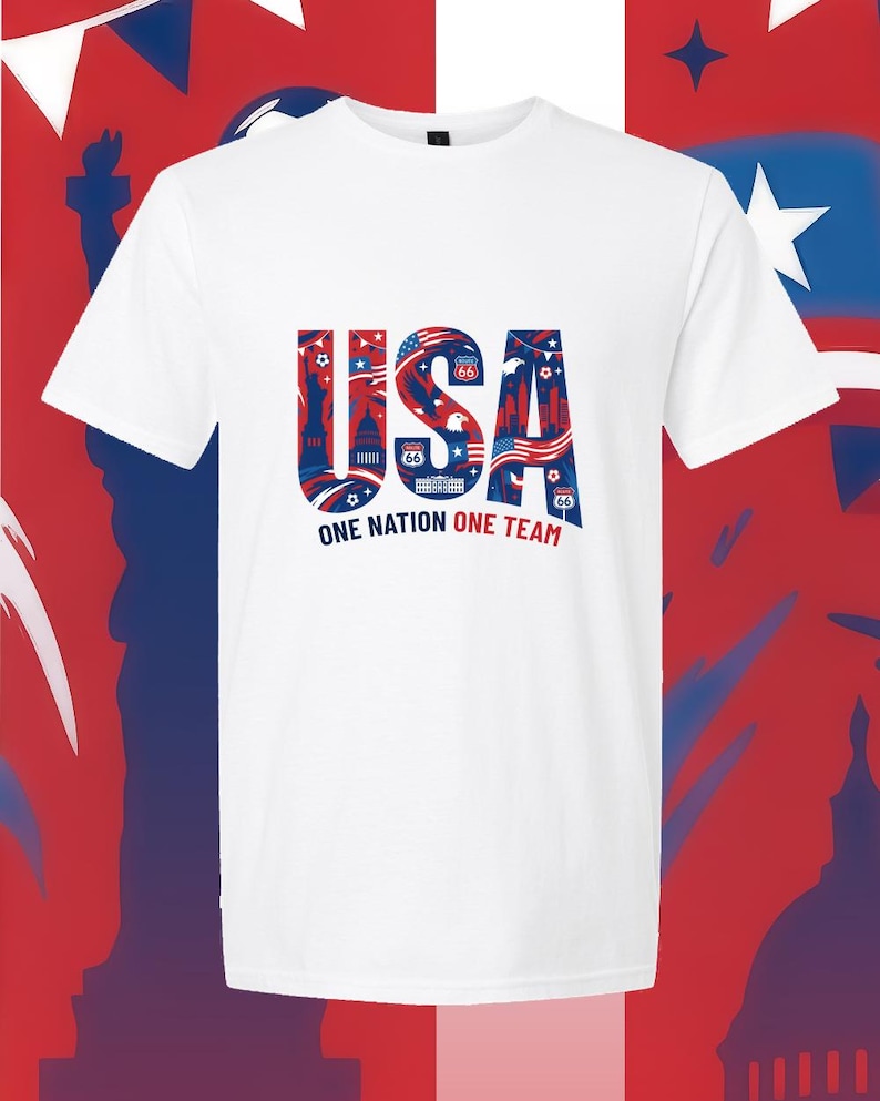 May include: A white short-sleeved t-shirt featuring a large graphic on the chest. The graphic displays the letters USA in blue, filled with red and white patriotic imagery including the Statue of Liberty, an eagle, and Route 66 signs. Below, the text reads ONE NATION ONE TEAM.