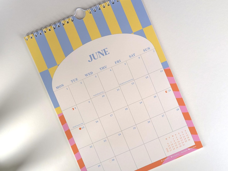 May include: A spiral-bound wall calendar for June, featuring a retro design with a yellow and blue striped background. The calendar has a white interior with dates and days of the week, and a colorful border.