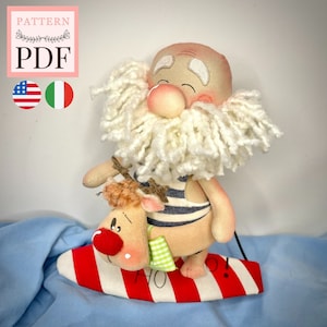 Può includere: Un giocattolo di peluche fatto a mano di un personaggio di Babbo Natale che cavalca un surf con una renna. Il giocattolo di Babbo Natale indossa un costume da bagno a righe blu e bianche e ha una barba bianca. La renna indossa un costume da bagno verde e bianco. Il surf è rosso e bianco con la scritta "HO!" su di esso.
