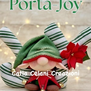 May include: A plush elf doll with a green hat and red collar, featuring small gold bells, positioned between two green and white striped fabric candy canes. A red poinsettia flower is attached to the right side. Text reads Porta-Joy Catia Celani Creazioni.