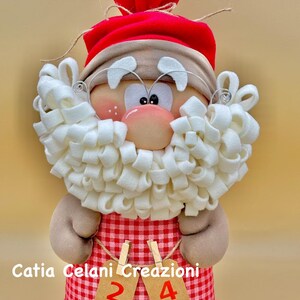 May include: A red and white gingham fabric Advent calendar with a Santa Claus figure. The Santa Claus figure has a white beard, a red hat, and a brown face. The calendar has the numbers 2 and 4 on it.