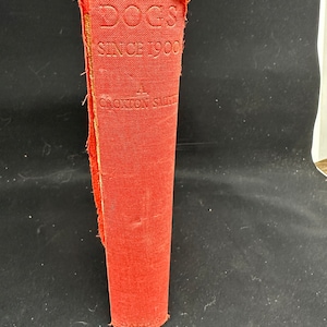 May include: A red hardcover book titled "Dogs Since 1900" by  "A. Croxton Smith" with the publisher "Dakers" printed on the bottom.