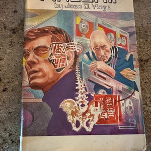 May include: A book cover with the title "FIRESHIP" by Joan D. Vinge. The cover features a colorful illustration of a man with a mechanical device attached to his head, a skeletal spine, and a futuristic cityscape in the background.