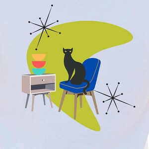 May include: A white t-shirt with a black cat sitting on a blue chair. The cat is in front of a green boomerang shape with a side table and stacked colorful bowls. There are black starbursts on either side of the design.
