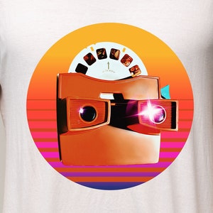 May include: A white t-shirt with a retro-style graphic of a vintage view-master toy. The graphic features a red and orange color scheme with a circular design and a sunset background.