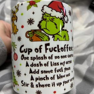 May include: White ceramic mug with a grumpy green character in a Santa hat. The mug features the text "Cup of Fuckoffee" and humorous instructions. Decorated with festive red and green accents.