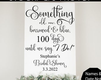 May include: White sign with black calligraphy text: "Something old, new, borrowed & blue, 100 days until we say 'I Do!'" with "Stephanie's Bridal Shower" and the date. The sign is on a wooden easel, decorated with greenery.