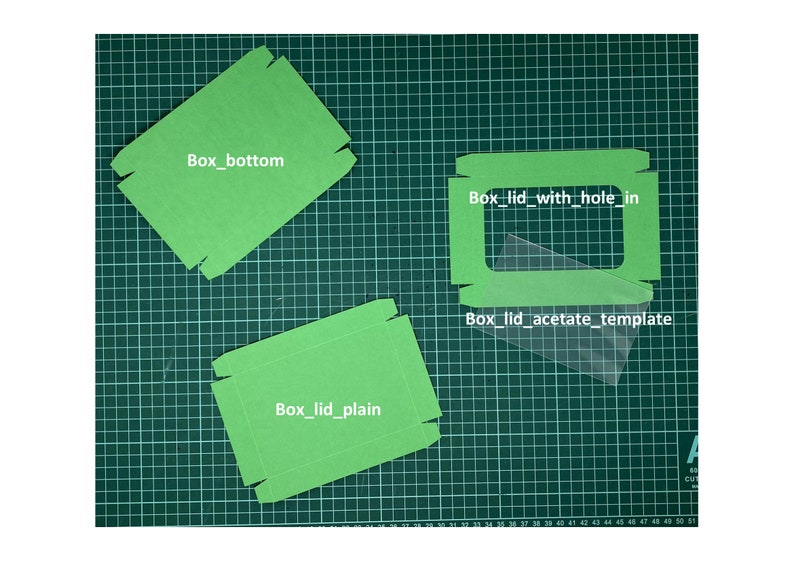 May include: Three green cardboard box templates on a green cutting mat. The templates are labeled "Box_bottom", "Box_lid_plain", and "Box_lid_with_hole_in". A clear acetate template is also visible, labeled "Box_lid_acetate_template".