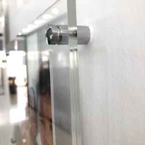May include: A clear acrylic photo frame with a silver metal hanging hardware. The frame is hanging on a white wall. A photo of a person is visible inside the frame.