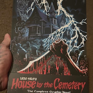 May include: A graphic novel box set titled "House by the Cemetery" by Lucio Fulci. The cover art features a haunted house, lightning, and a bloody hand holding a knife. The box set includes four books and is based on the classic film.