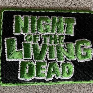 May include: Green and white embroidered patch with the text "Night of the Living Dead" on a black background.
